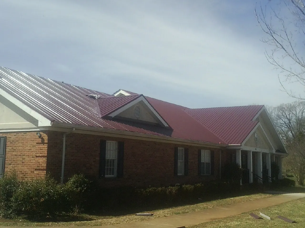 Red metal roof with gabled entries on a long brick building, from a Hail Damage Roof Repair job in Bath